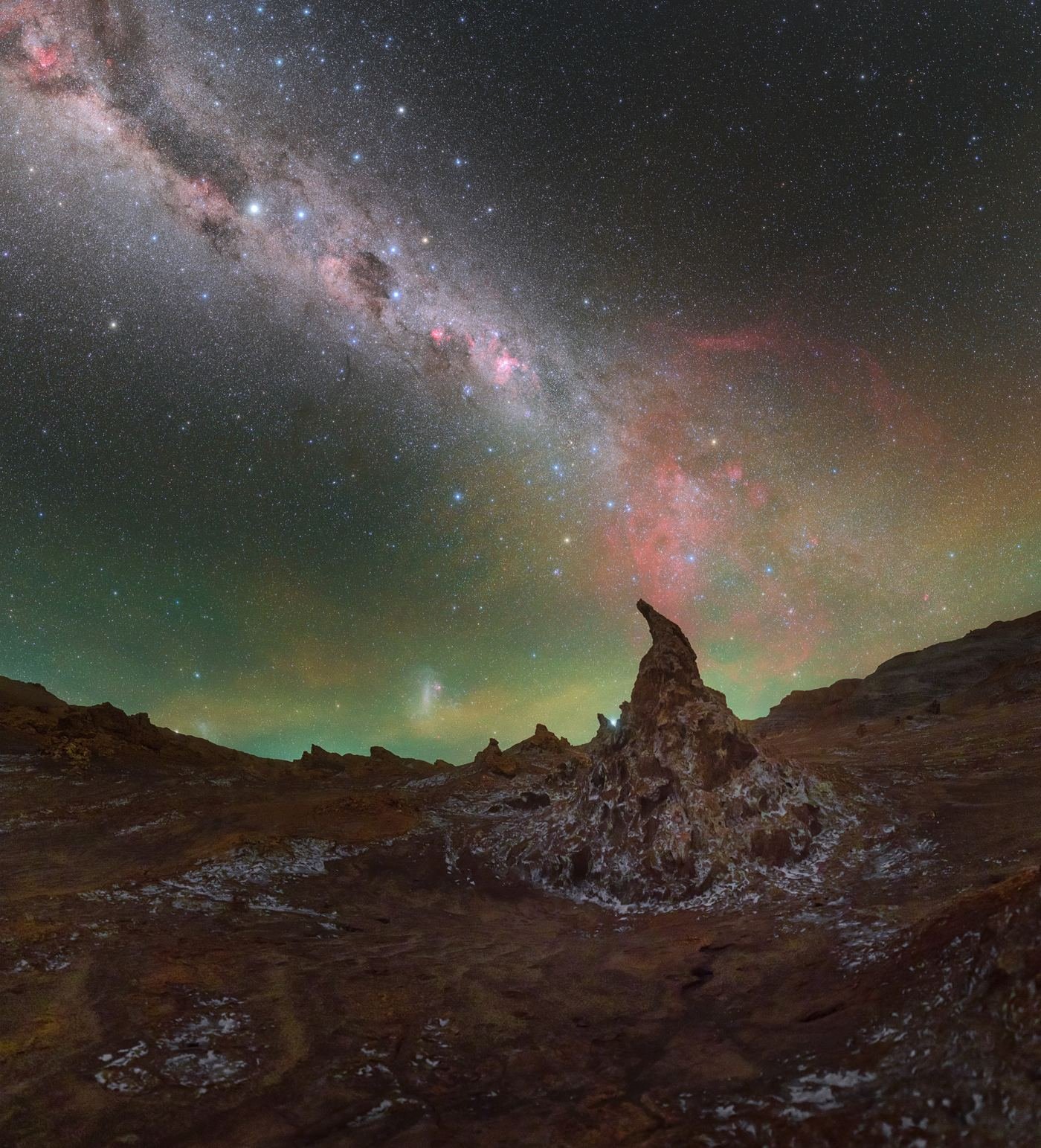 A rock spire under the Milky Way with green airglow along the horizon