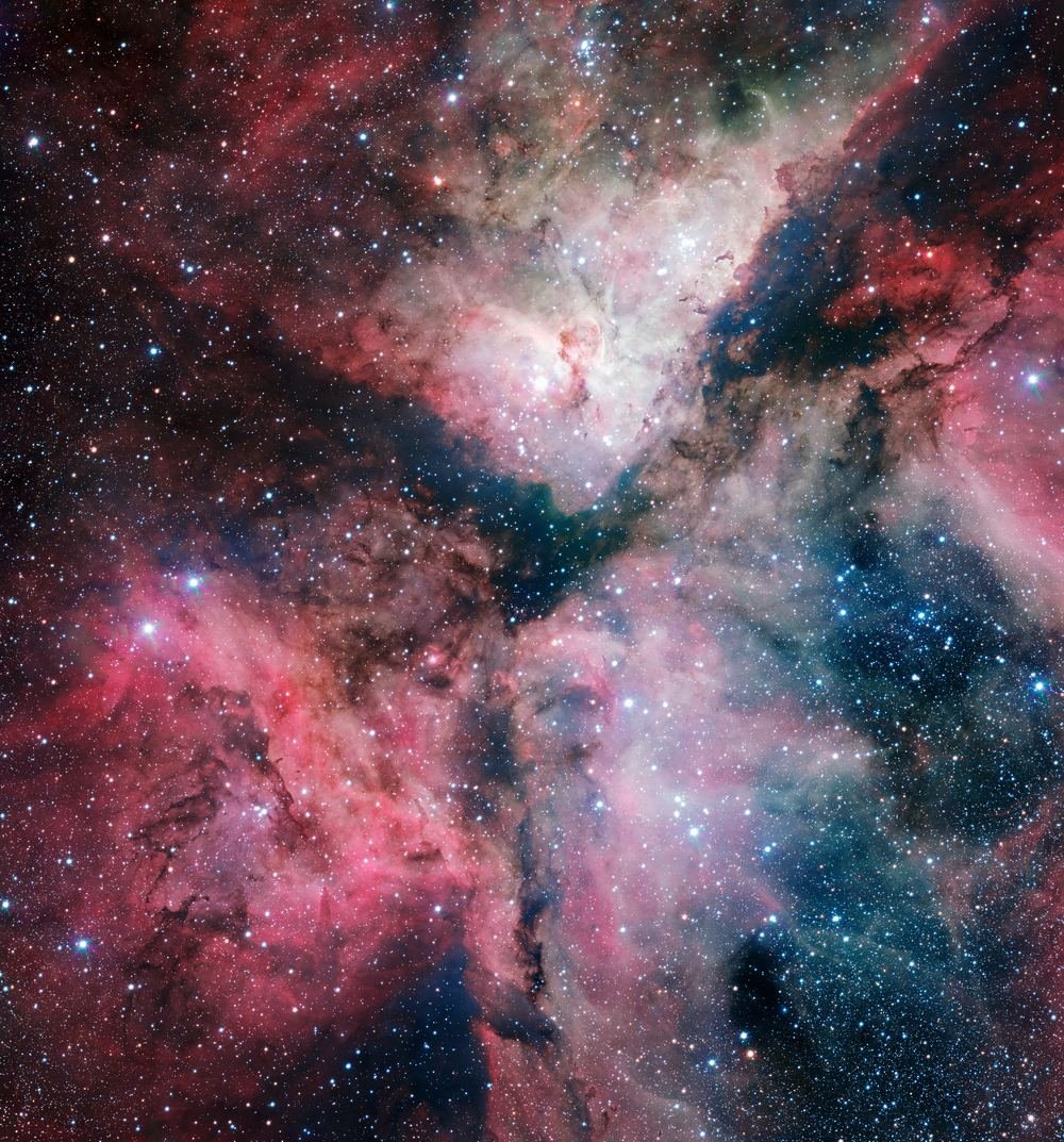 The Carina Nebula: glowing pink and blue clouds of gas threaded with dark dust lanes and bright stars, photographed by a survey telescope