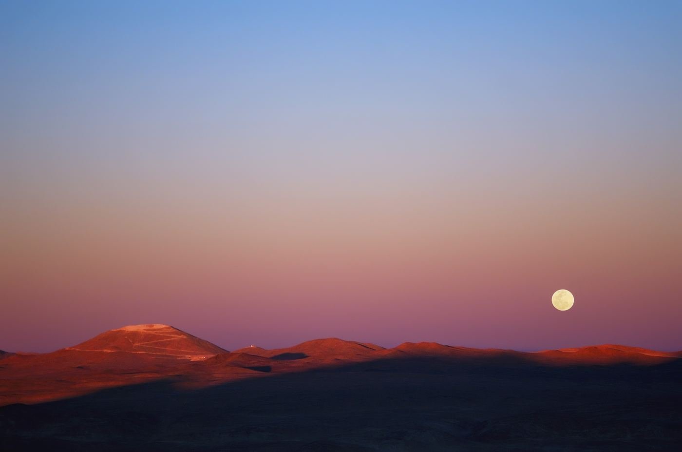 A full moon rising over a dark mountain ridge at twilight