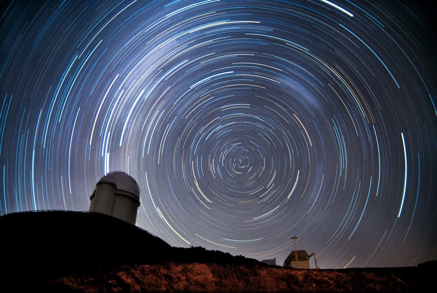 Star trails circling over a dark hill as the night turns